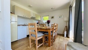 Una cocina compacta con armarios blancos, una mesa de comedor de madera con sillas y una ventana con cortinas.
