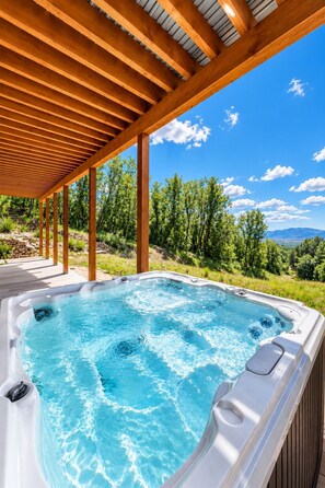 Un bain à remous sous une pergola en bois, offrant une vue dégagée sur un paysage montagneux.