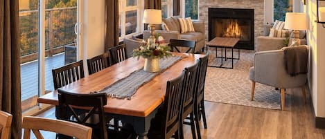 A spacious living room with a fireplace, a dining area with a wooden table and chairs, and a balcony with large windows.