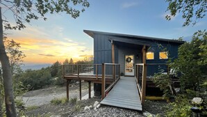 A modern cabin with a wooden deck and a small porch, surrounded by trees and a gravel path. - Your Hideaway Surrounded by the Breathtaking Beauty of Utah's Natural Landscape (Fairview)