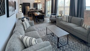A spacious living room with a gray sofa, a coffee table, and a ceiling fan. There is a dining area in the background with a chandelier. - Your Hideaway Surrounded by the Breathtaking Beauty of Utah's Natural Landscape (Fairview)