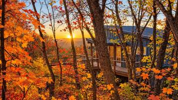 A cabin surrounded by autumn foliage with a view of the sunset.