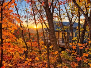 Une cabane entourée du feuillage automnal, avec vue sur le coucher du soleil.
