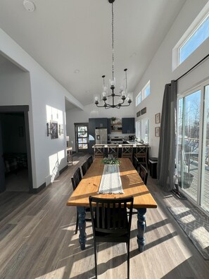Une salle à manger spacieuse avec une longue table en bois, des chaises noires et un lustre central.