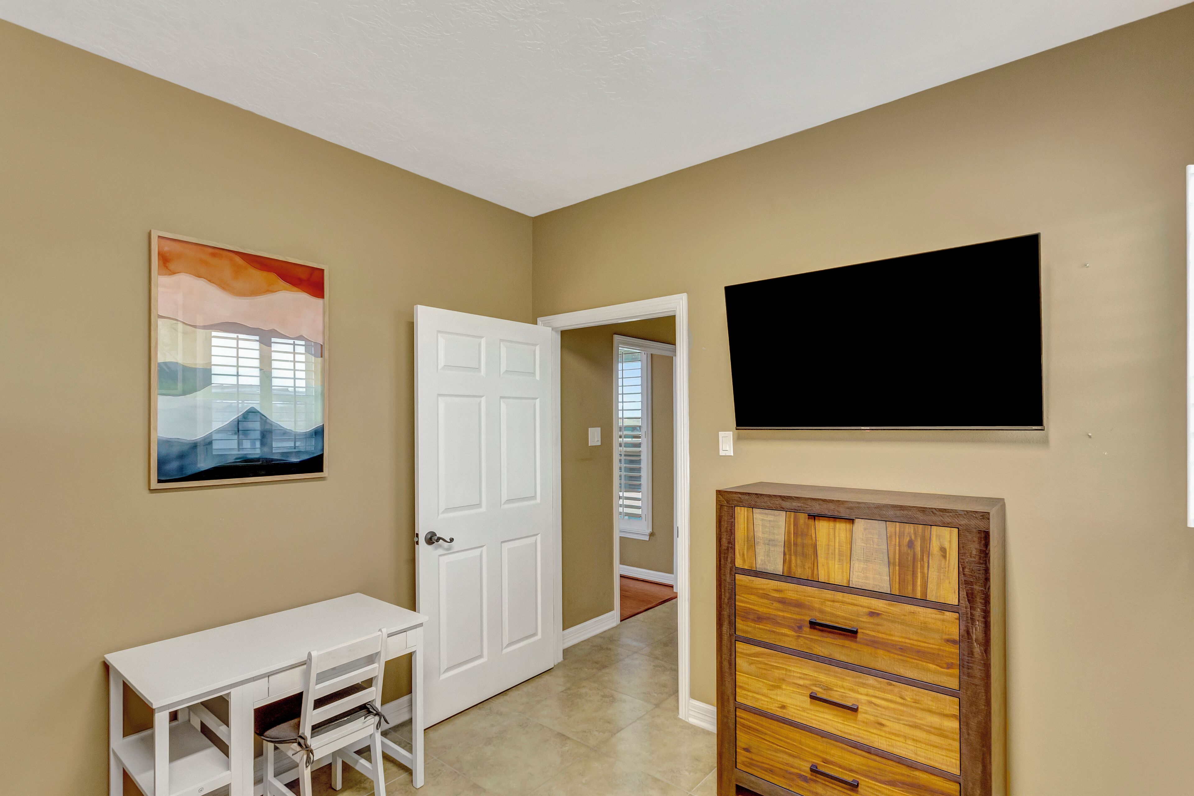 A hallway with a white door, a painting, a TV mounted on the wall, and a wooden cabinet.