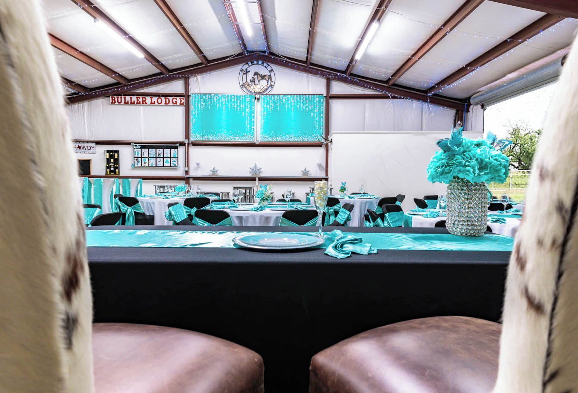 Een evenementenruimte met tenten, turquoise decoratie, en tafels gedekt voor diner, met een bord waarop 'BULER LODGE' staat.