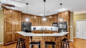 A kitchen with wooden cabinets, a central island with stools, stainless steel appliances, pendant lights, and a ceiling fan. - Countryside Texas Sanctuary Enjoy Sunrises & Sunsets, Grill, Firepit & Longhorns (Pattison)