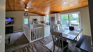 A spacious kitchen with wooden ceiling, white cabinets, and a dining area with a table and chairs.