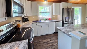 A modern kitchen with white cabinets, a stainless steel refrigerator, a built-in oven, and a wooden ceiling.