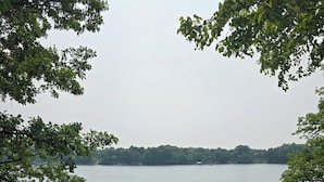 A lakeside patio with a table and chairs, a dock with a boat, and a view of the lake and trees.