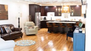 A modern kitchen with dark cabinets, a central island with bar stools, a refrigerator, and a dining area with a table and chairs.