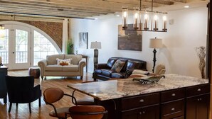 A spacious living area with a large wooden ceiling, a marble island, and a black leather sofa.