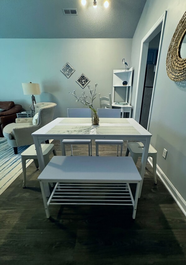 Un coin repas avec une table et un banc blancs, un vase orné de branches et une étagère murale décorative.