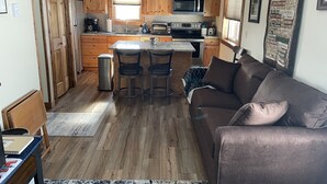 A compact kitchen with wooden cabinets, a central island with stools, a microwave, and a coffee maker. - Paradise Land Cabin A (Custer)