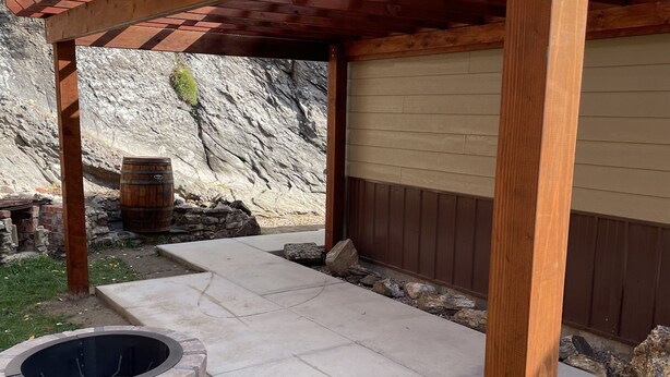A wooden pergola structure, a stone fire pit, and a concrete patio area. - Paradise Land Cabin A (Custer)