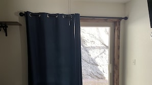 A bedroom with a bed, a window with a curtain, and a view of a rocky landscape. - Paradise Land Cabin A (Custer)