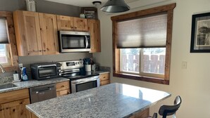 A kitchen with granite countertops, wooden cabinets, stainless steel appliances, and a large island with bar stools. - Paradise Land Cabin A (Custer)