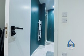 A modern interior with a white door, a hallway leading to a bathroom, and a visible shower area.