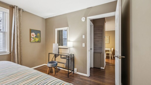 Un dormitorio con una cama, un escritorio con una silla, una ventana y una puerta que da a otra habitación.