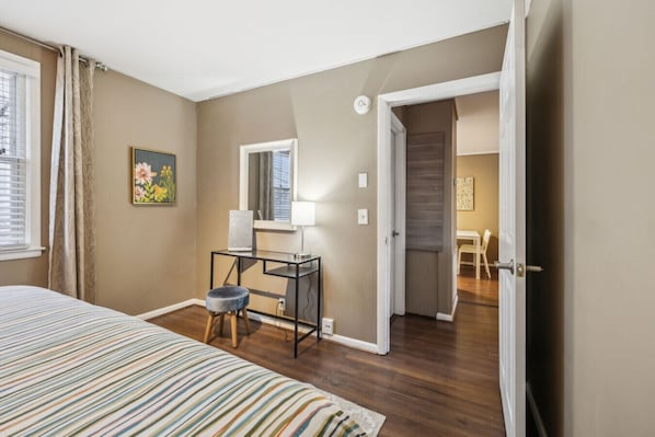 A bedroom with a bed, a desk with a chair, a window, and a door leading to another room.