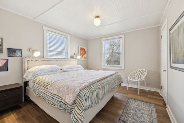 A bedroom with a bed, two windows, a chair, and a nightstand.