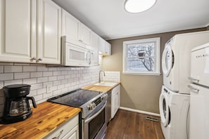 A compact kitchen with white cabinets, a black induction cooktop, a built-in microwave, a stainless steel oven, a sink, and a white washing machine.