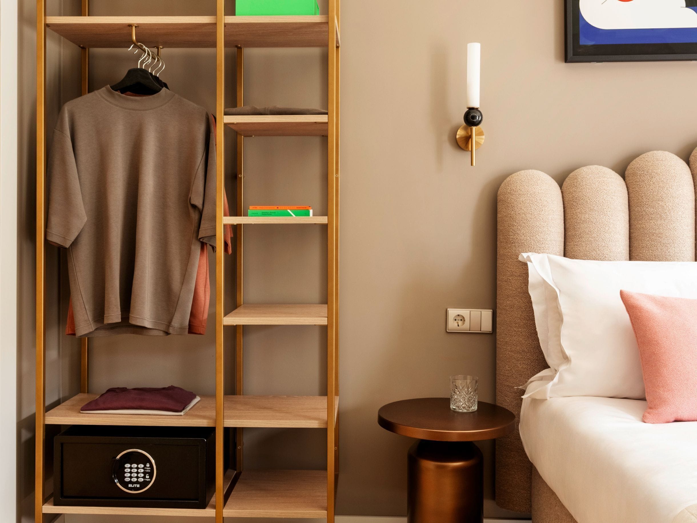 A hotel room with a wardrobe, a bedside table, a lamp, and a bed with pillows.