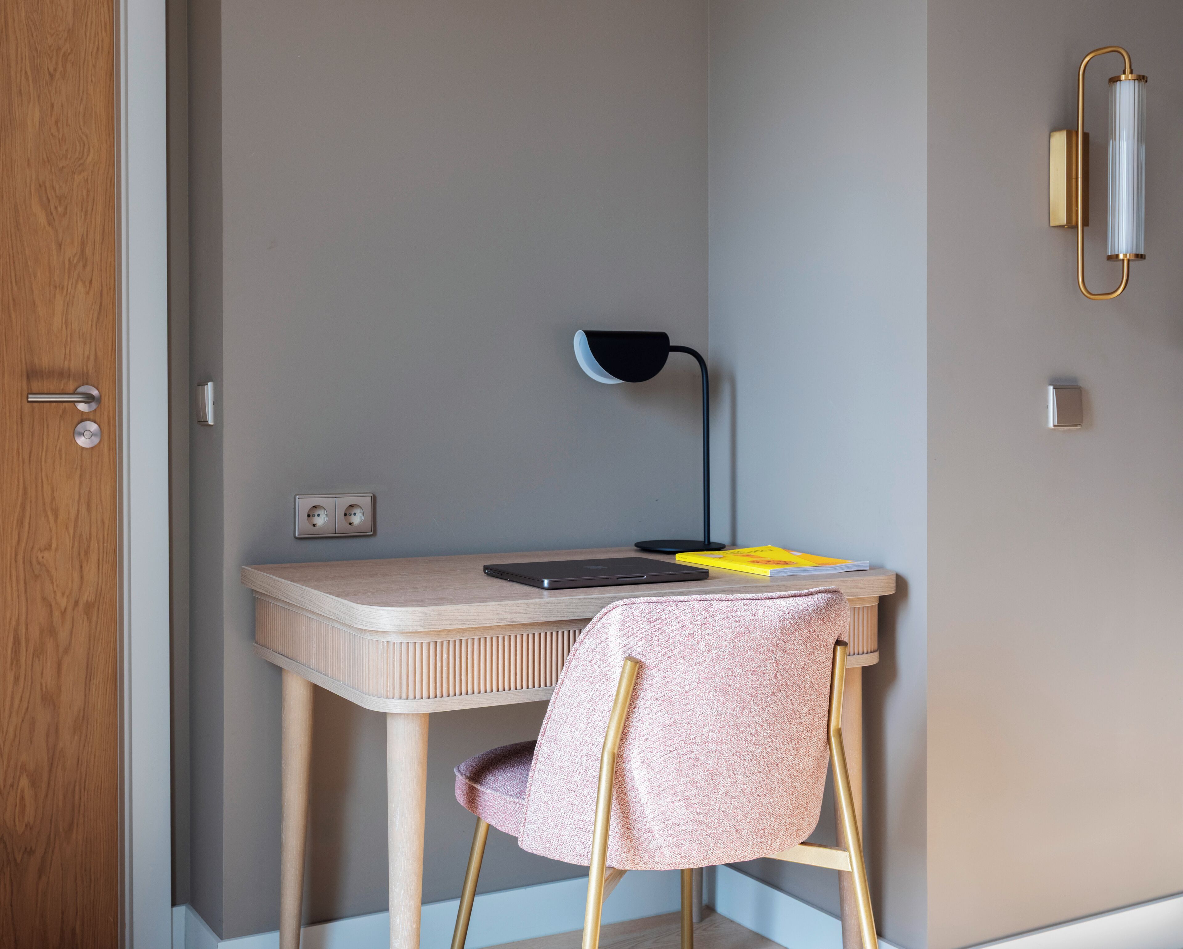 Une petite pièce moderne, dotée d’un bureau en bois, d’une chaise, d’une lampe et d’un luminaire fixé au mur.
