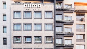 Un hôtel moderne avec une façade en marbre, de nombreux balcons et une entrée bien visible, avec une voiture garée devant.