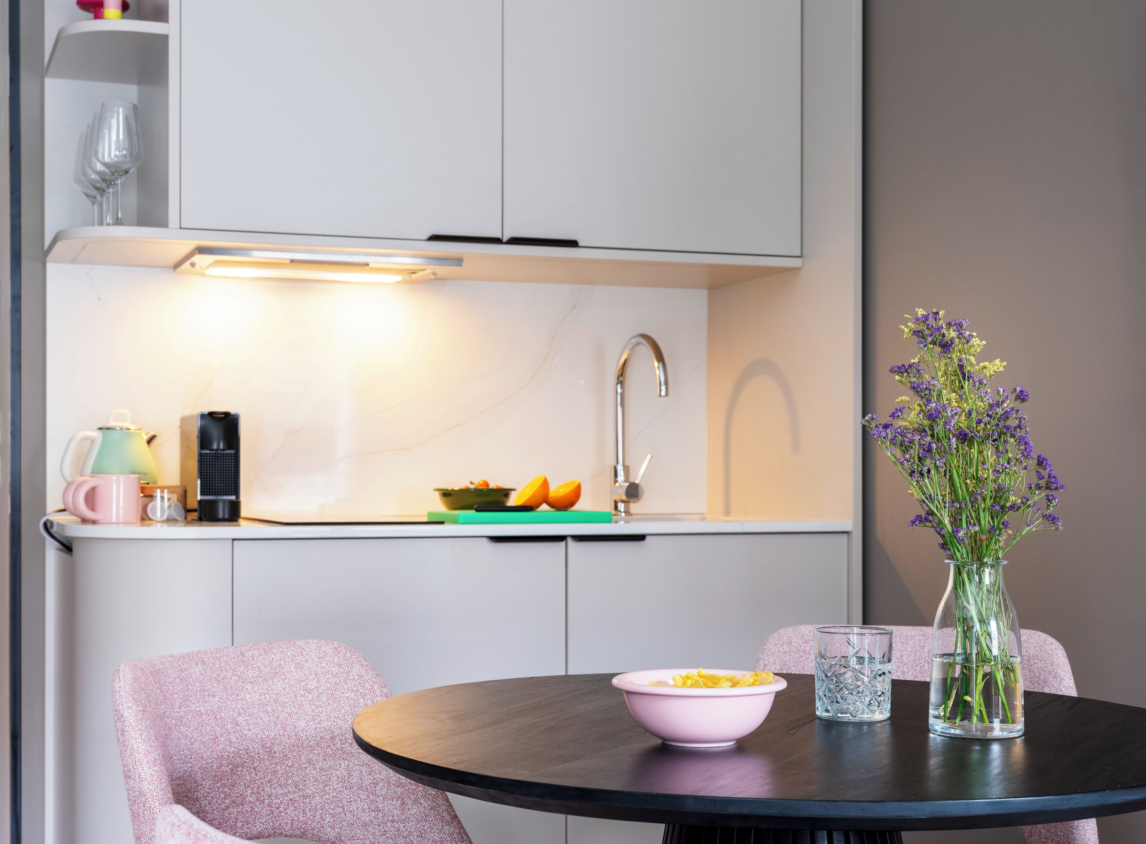 A modern kitchen with a built-in oven, a sink, and a dining area with a table and chairs.