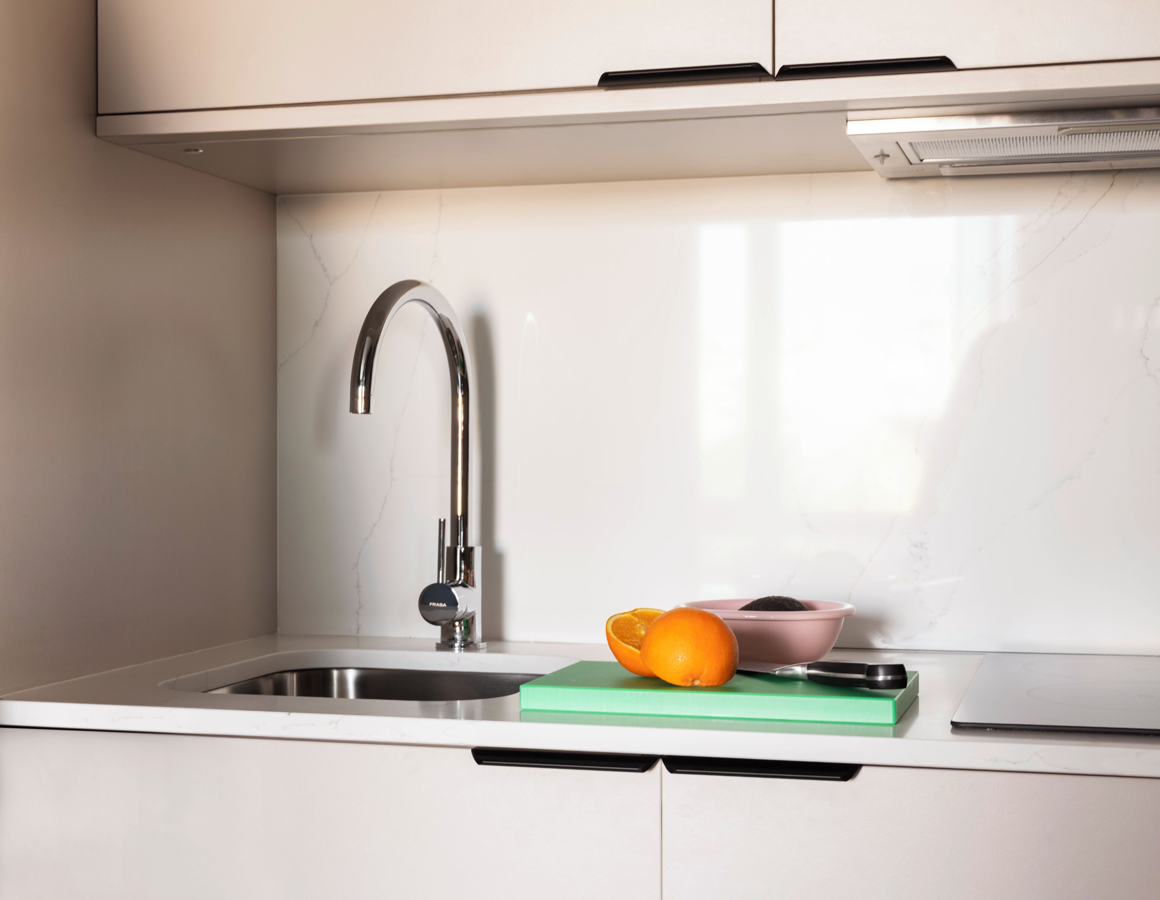 Eine moderne Küche mit Spüle aus Edelstahl, einem Wasserhahn, einer grünen Schneidebrett und einer Schüssel mit einer Orange.