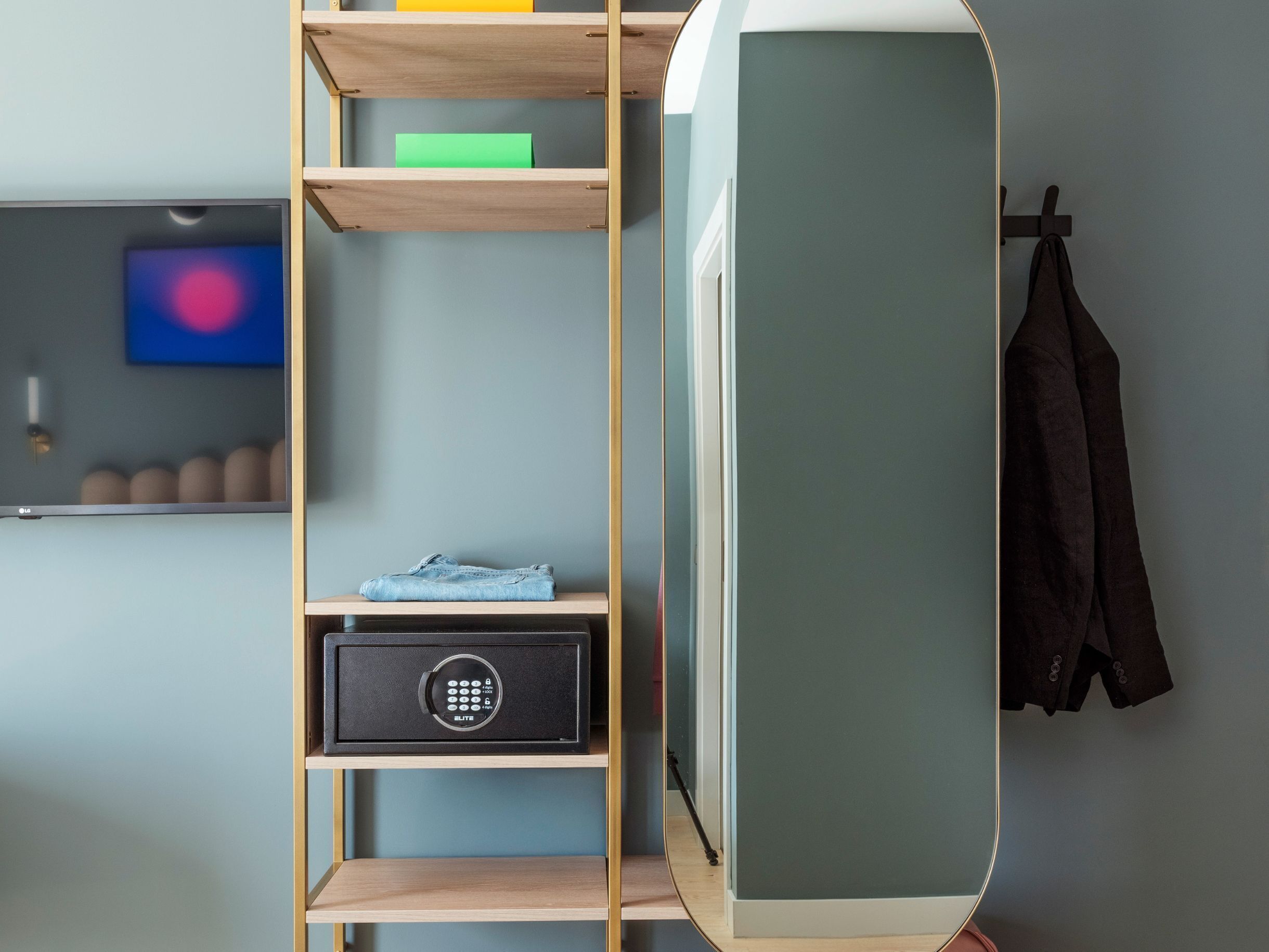 Ein Zimmer mit einer Holzregaleinheit, einem schwarzen Safe, einem Fernseher und einem Mantel an einem Haken.
