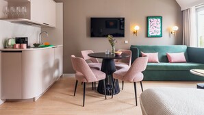 Une cuisine moderne avec un coin repas, un canapé vert et un téléviseur fixé au mur.