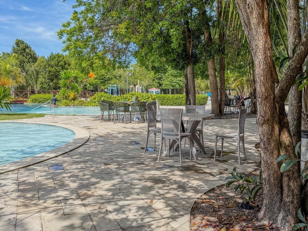 Un espace aménagé au bord de la piscine, avec une piscine aux formes arrondies, des sièges extérieurs et des arbres.