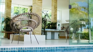 A modern indoor pool area with a unique spiral chair, glass walls, and a view of greenery.