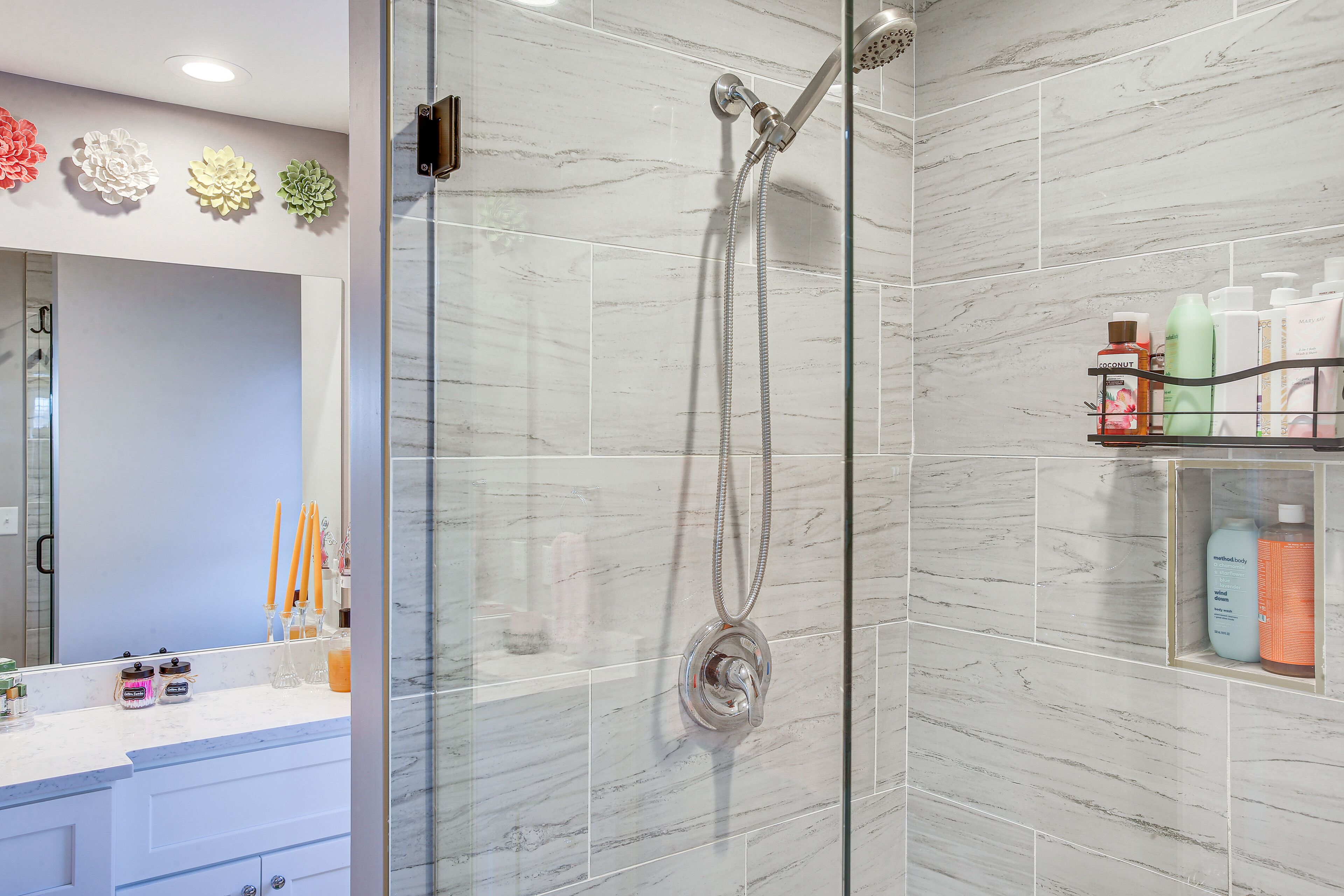 Une salle de bain moderne avec une douche à parois de verre, des carreaux de marbre et un meuble-lavabo avec des articles de toilette.