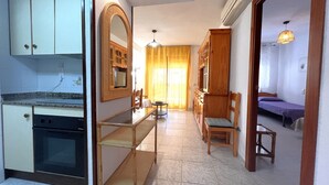 Eine kompakte Küche mit Einbauofen, ein Essbereich mit Glastisch und eine kleine Sitzecke mit Sessel und Sofa.