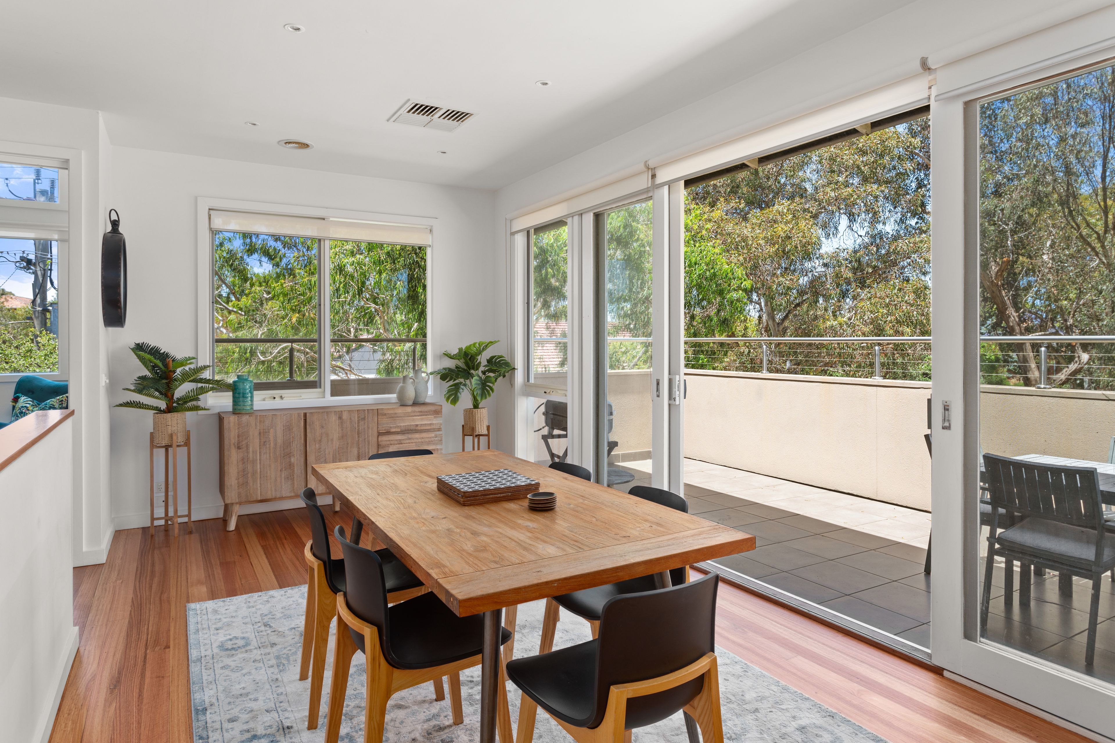 A modern dining area with a wooden table and chairs, large windows, and a view of the outdoors.