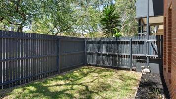 A fenced backyard with grass and a tree.