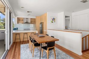 A modern kitchen with a central island, wooden cabinets, and a dining area with a table and chairs. - Flora  Pet Friendly Coastal Hampton Retreat (Hampton)