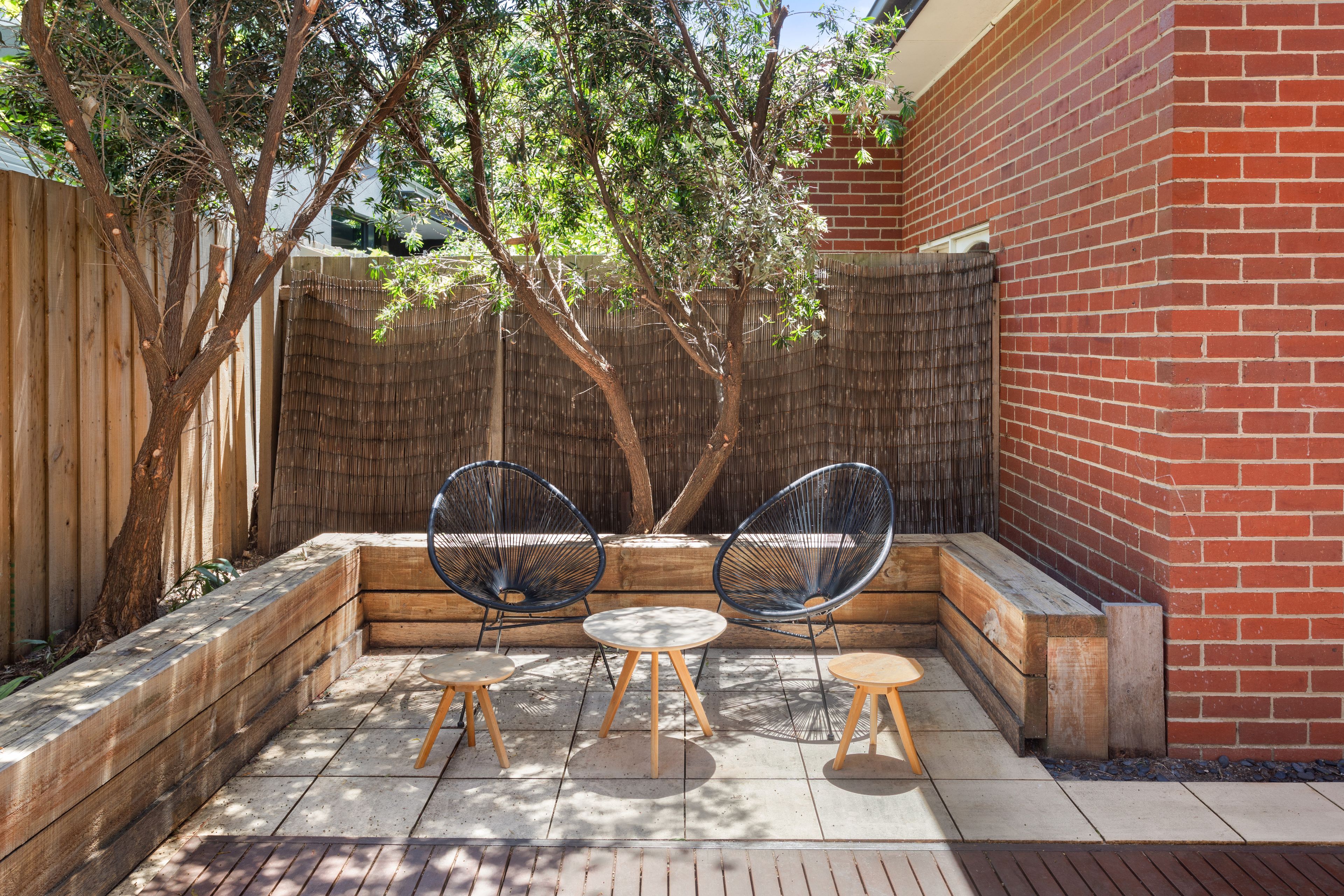 An outdoor seating area with two chairs and a table, surrounded by a wooden fence and a brick wall.