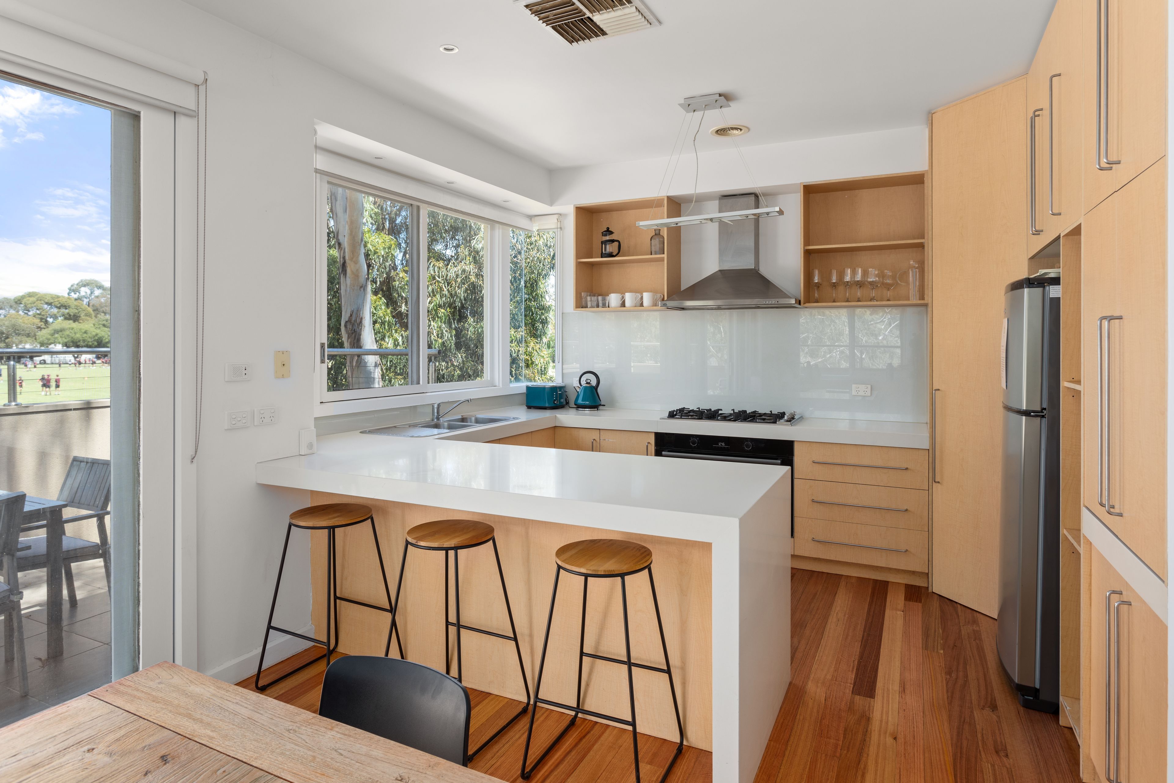 A modern kitchen with a large island, bar stools, a built-in oven, and a refrigerator.