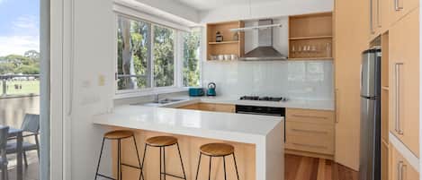 A modern kitchen with a large island, bar stools, a built-in oven, and a refrigerator.