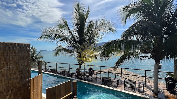 A pool area with wooden deck chairs and a view of the sea. - Residencial Solariun Ilhabela (Ilhabela)