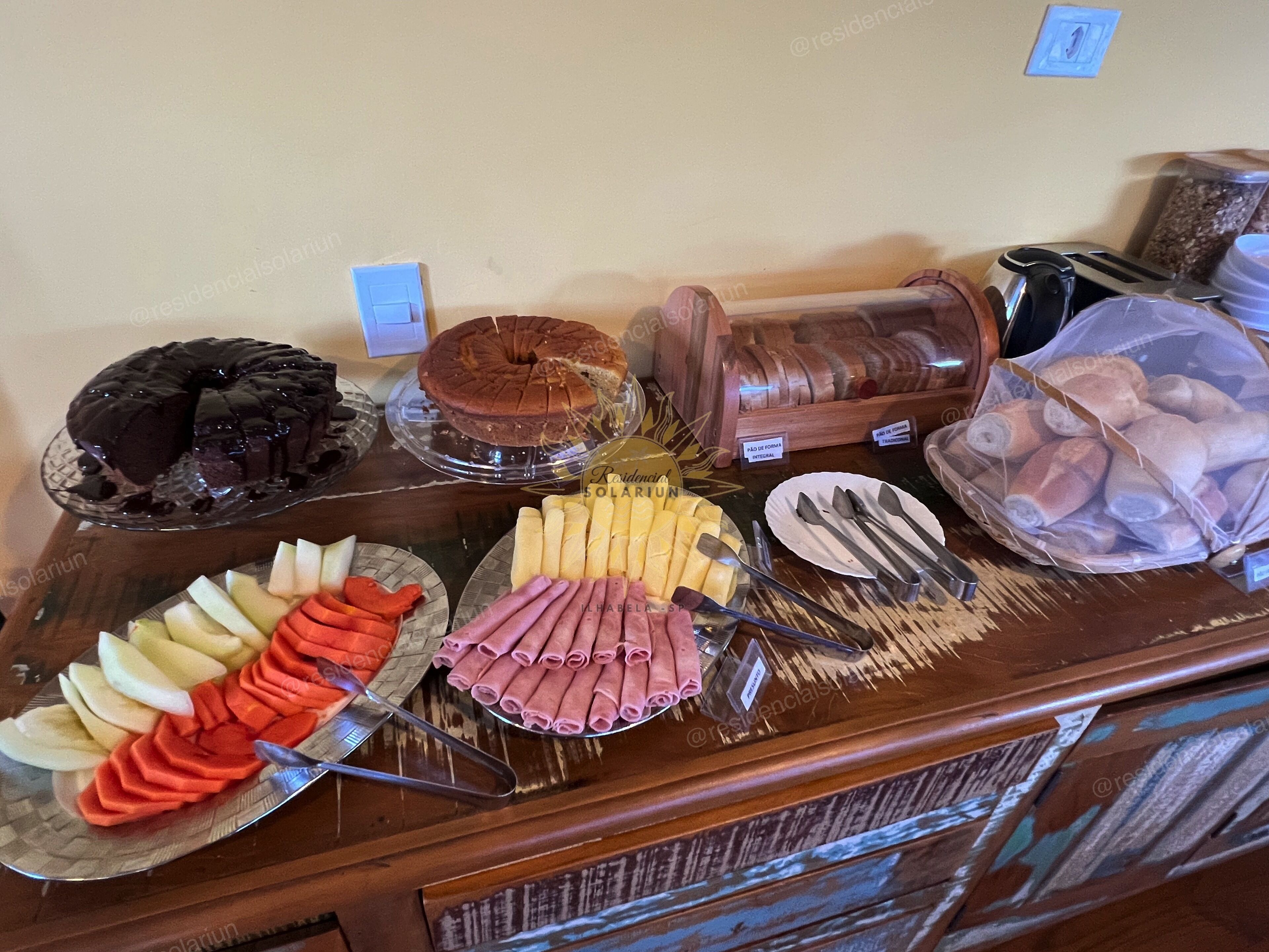 Un bufé con diversos alimentos, incluyendo un pastel de chocolate, un pastel glaseado y una variedad de frutas y carnes.