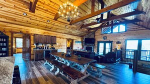 Un intérieur de chalet en bois spacieux, comprenant une grande table à manger, un coin cuisine et un espace salon.