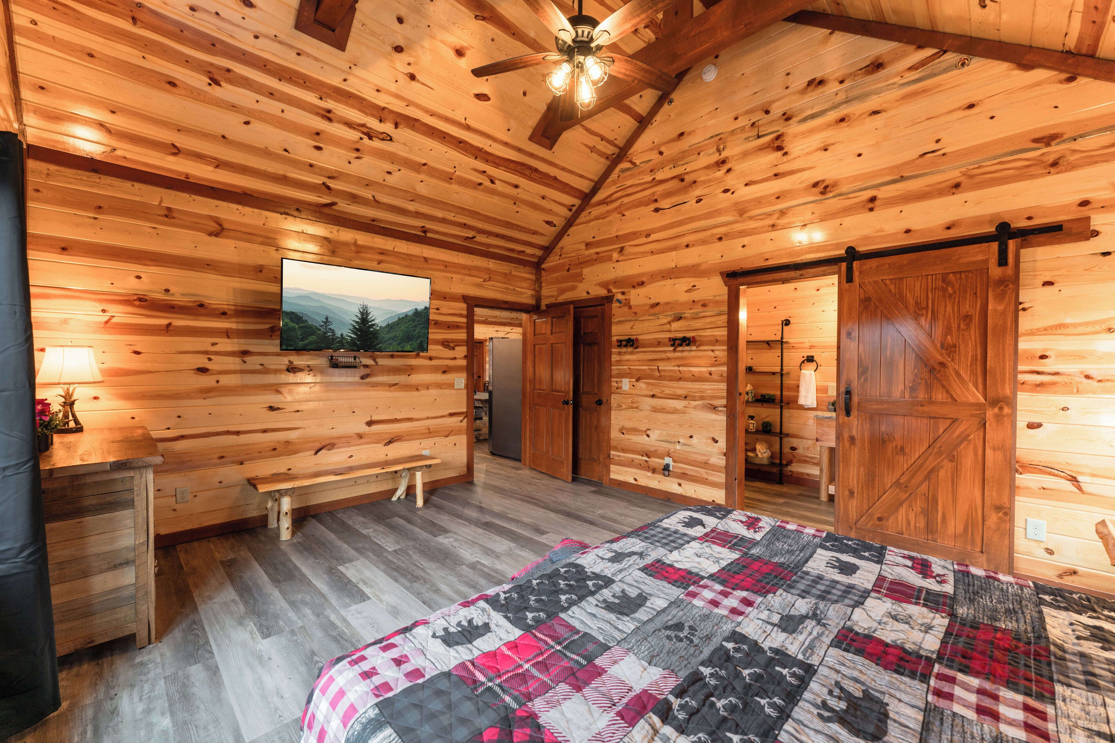 Un dormitorio de cabaña de troncos con una cama, un televisor, un banco de madera y una puerta corrediza.