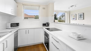 Uma cozinha moderna com armários brancos, micro-ondas, chaleira e janela com vista para uma casa.