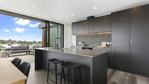 Une cuisine moderne avec des meubles de couleur sombre, un grand îlot central doté de tabourets et une vue sur l’extérieur.