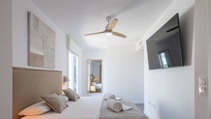 Una habitación de hotel moderna con una cama grande, un ventilador de techo, un televisor de pantalla plana y un espejo amplio.